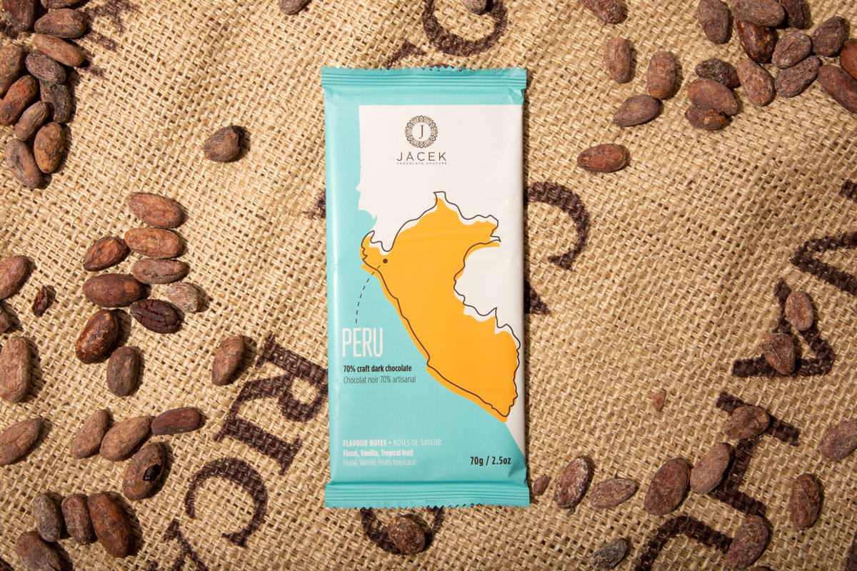 Image of A teal chocolate bar wrapper, picturing an illustrated depiction of the country Peru, sits on a burlap sack among scattered cocoa beans.